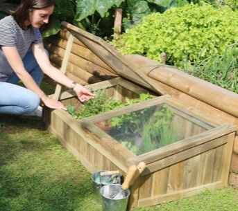 A woman using her cold frame by a raised bed